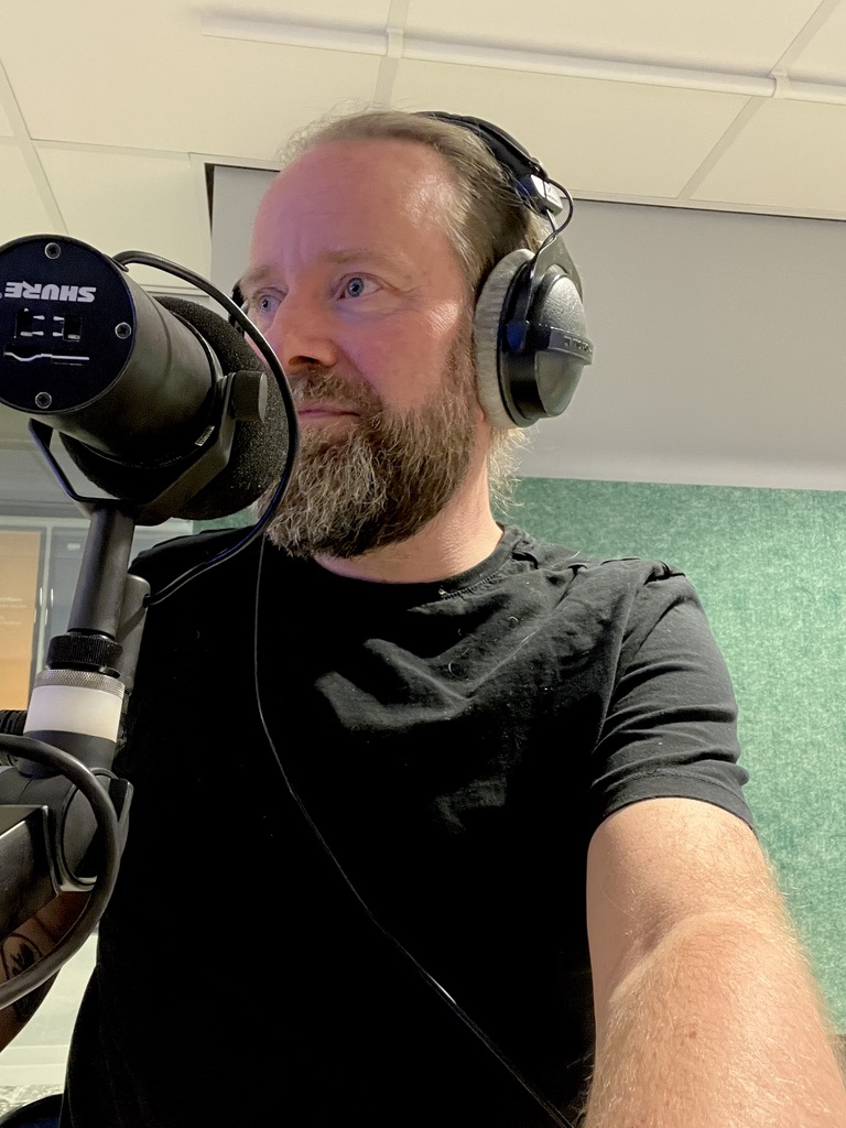 Perry recording a podcast in a studio with a Shure microphone and headphones
